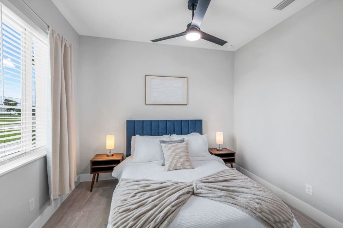 Helles Schlafzimmer mit blauem Kopfteil, zwei Nachttischen und Fensterblick.