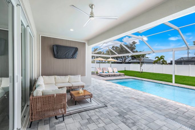 Moderne, helle Terrasse mit Lounge-Möbeln und Pool im Hintergrund.