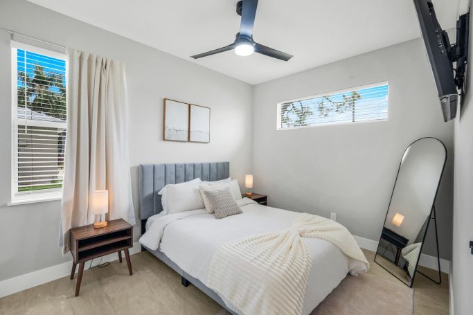 Helles Schlafzimmer mit Doppelbett, Spiegel, Fenster und moderner Beleuchtung.