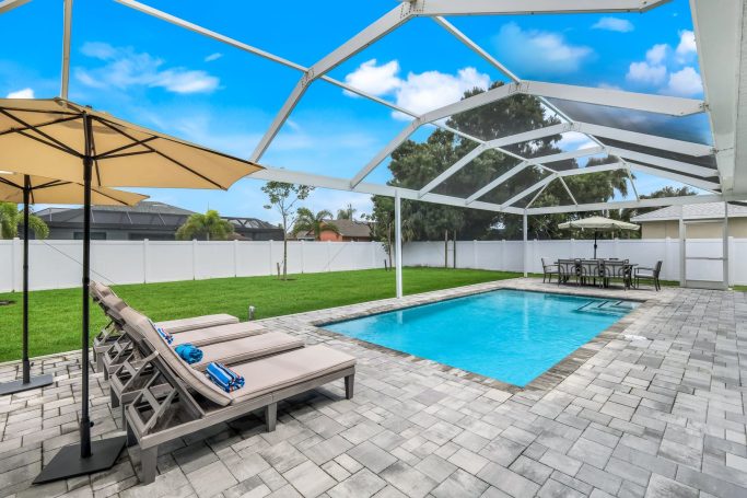 Modern Garten mit Pool, Liegen und Sonnenschirmen, umgeben von Rasenfläche.